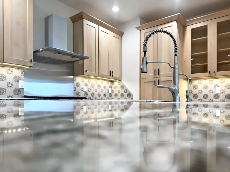 Maple shaker-style kitchen with a patterned tile backsplash, stainless chimney range hood and glass-front upper cabinets