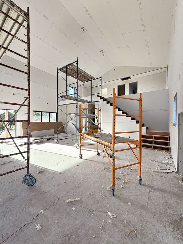 Open-concept living area at drywall stage with a custom staircase and scaffolding