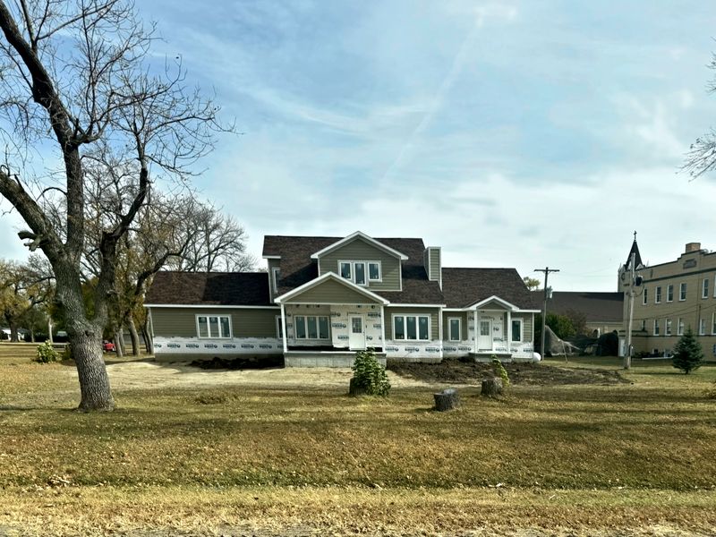 Two-story home with siding going on over house wrap, surrounded by mature trees